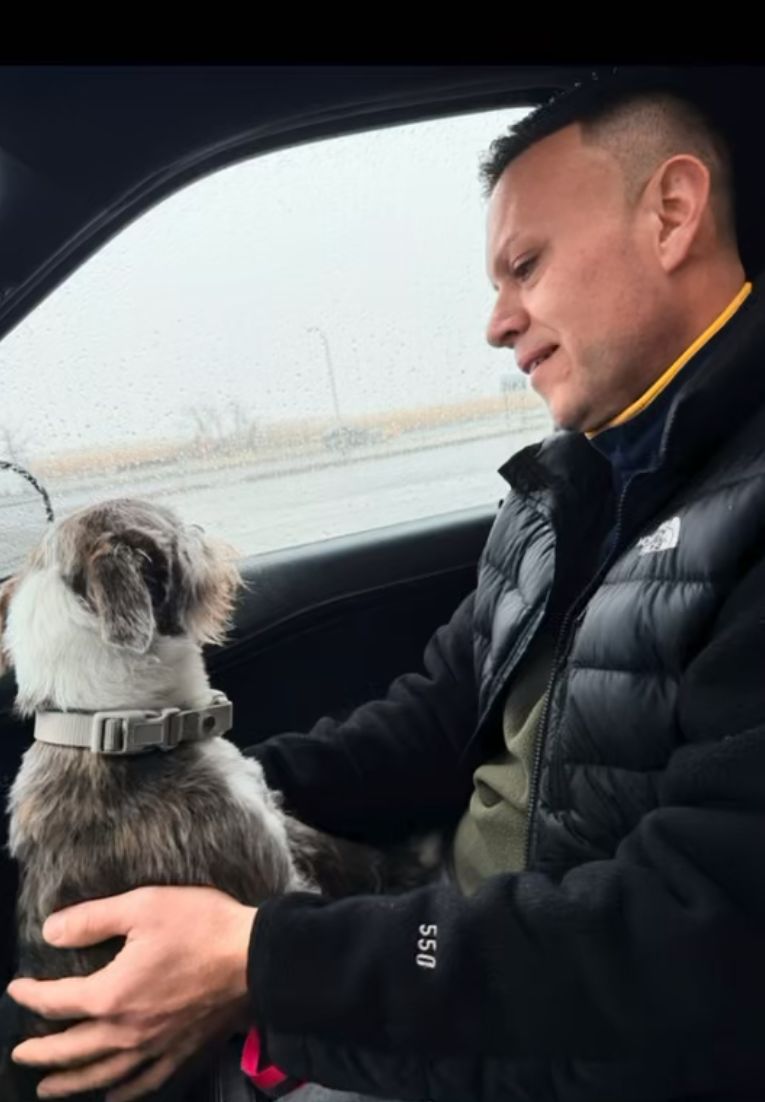 A man sits in a car on a rainy day with a small dog from a dog rescue in Atlanta on his lap, both looking out the window.